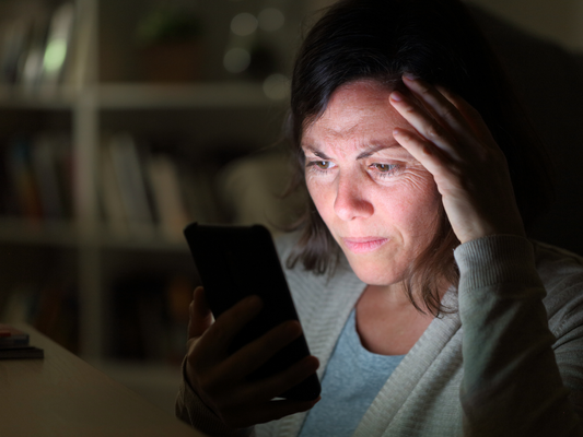 Woman staring at phone with worried expression, representing stress and sleepless nights