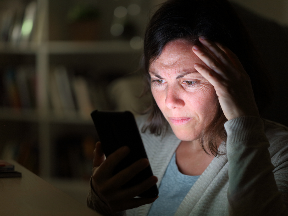 Woman staring at phone with worried expression, representing stress and sleepless nights